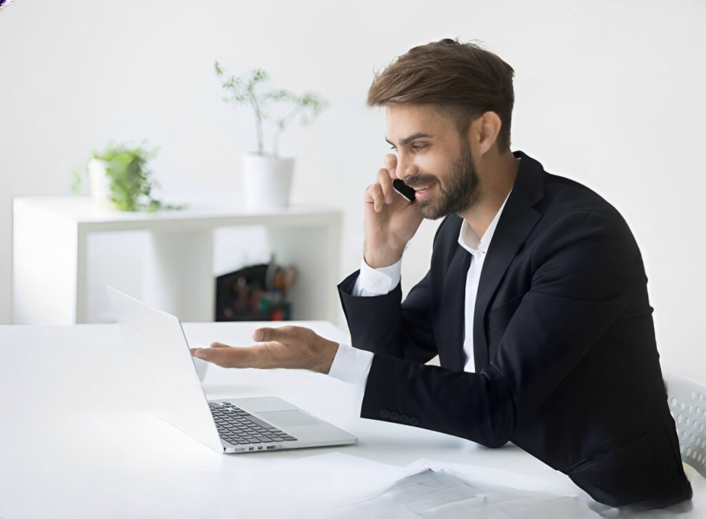 stock-photo-smiling-successful-businessman-in-suit-talking-on-phone-using-laptop-sitting-at-office-workplace