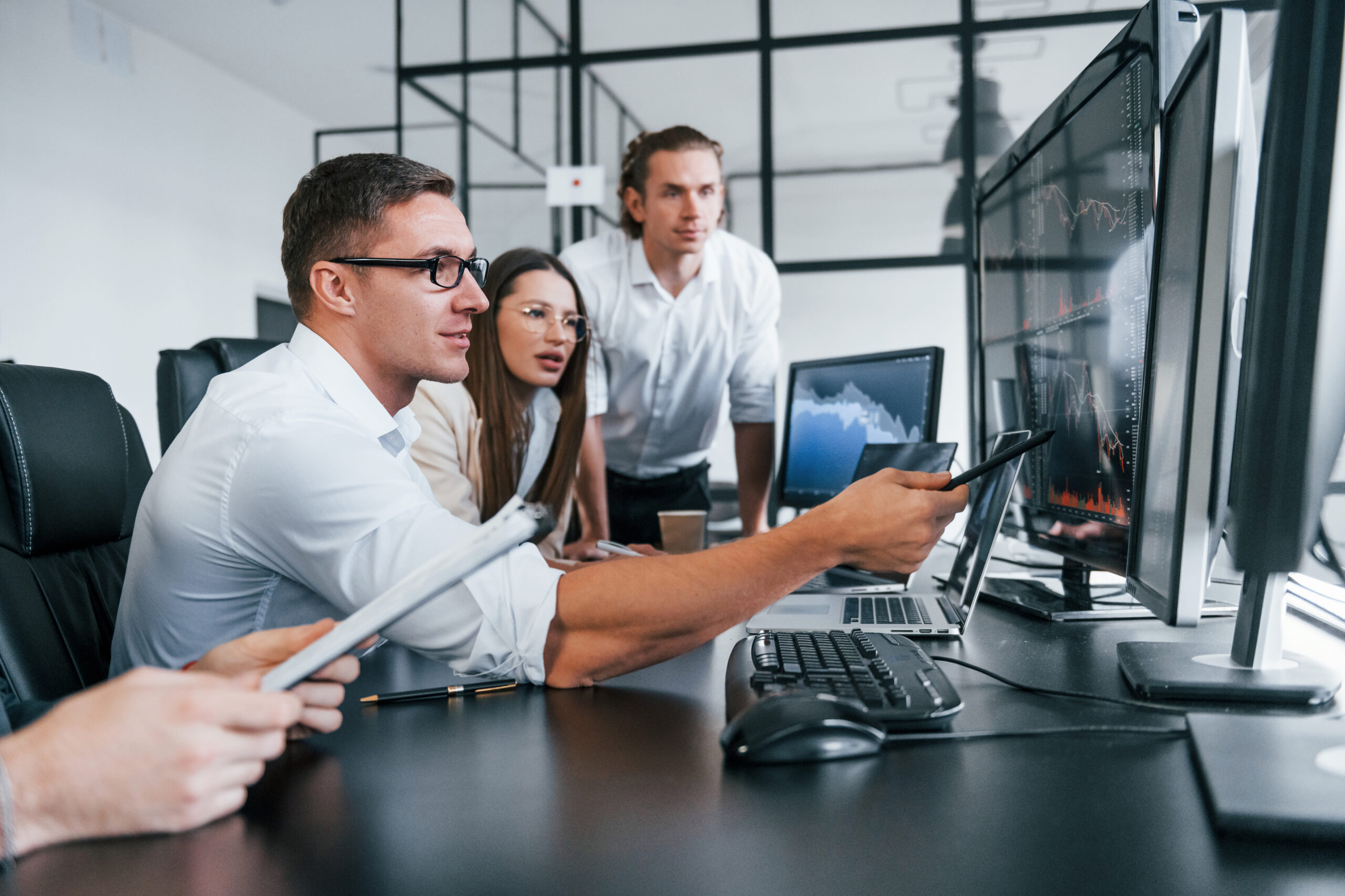 Sitting by the table. Team of stockbrokers works in modern office with many display screens.