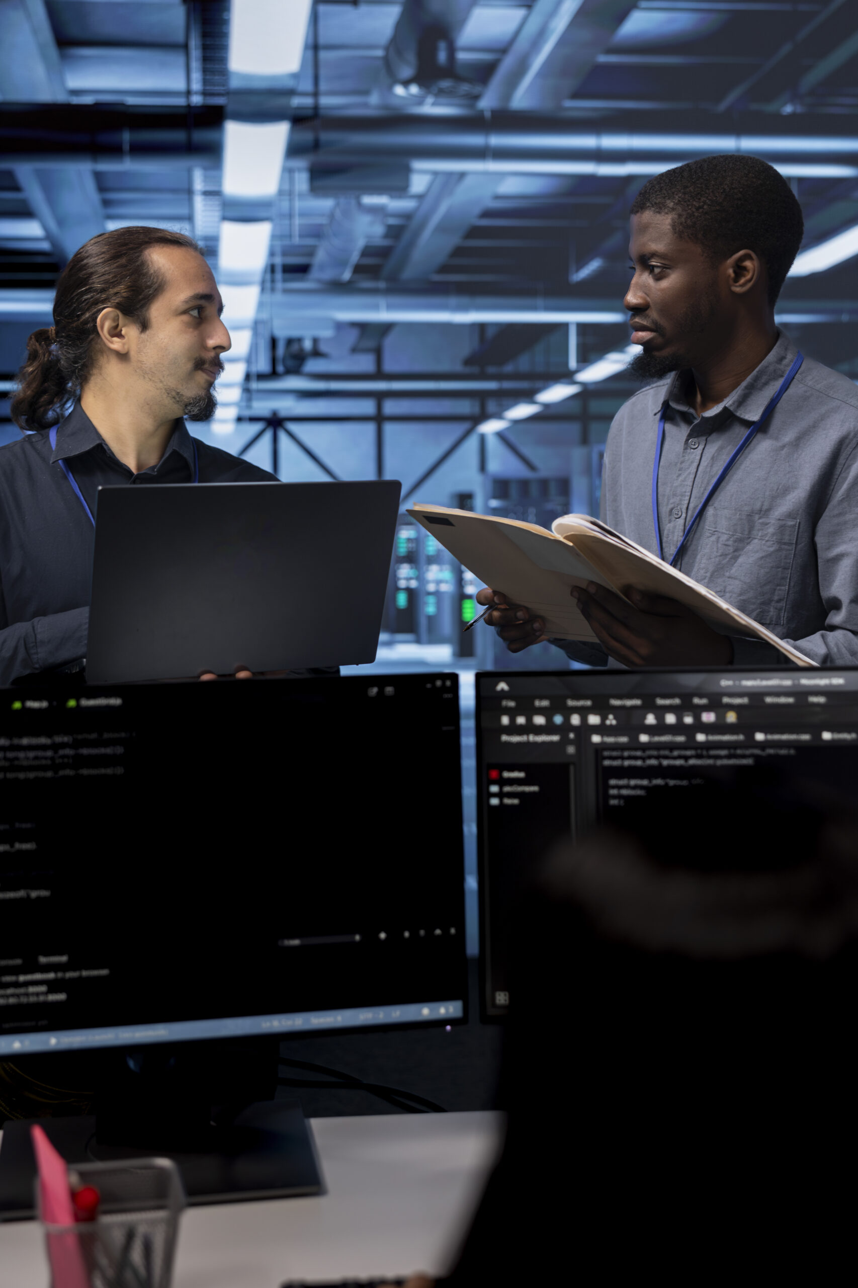 Manager getting feedback from engineer while overseeing data center, looking for firewall misconfigurations. Supervisor talking with workers in server room, asking about systems bottlenecks